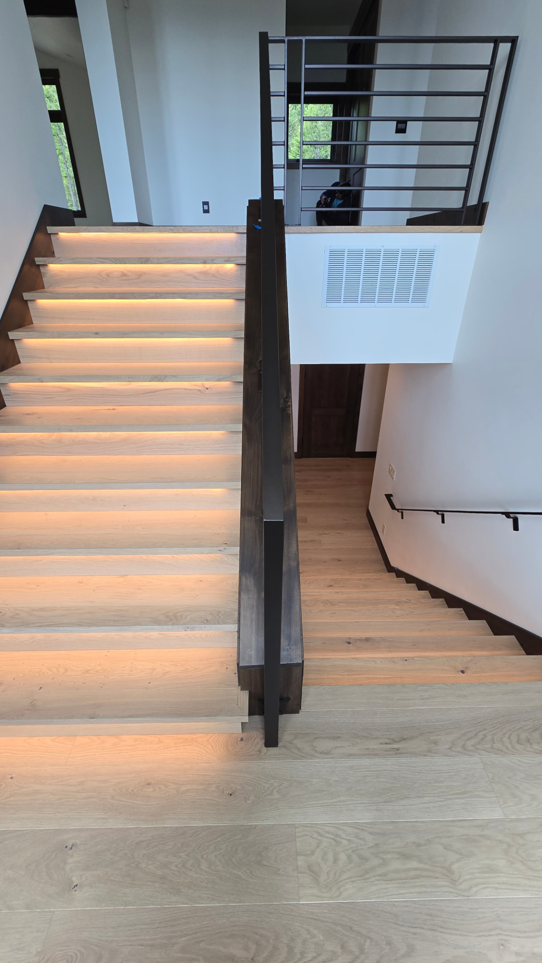 Backlit oak stair run beside a dark timber post