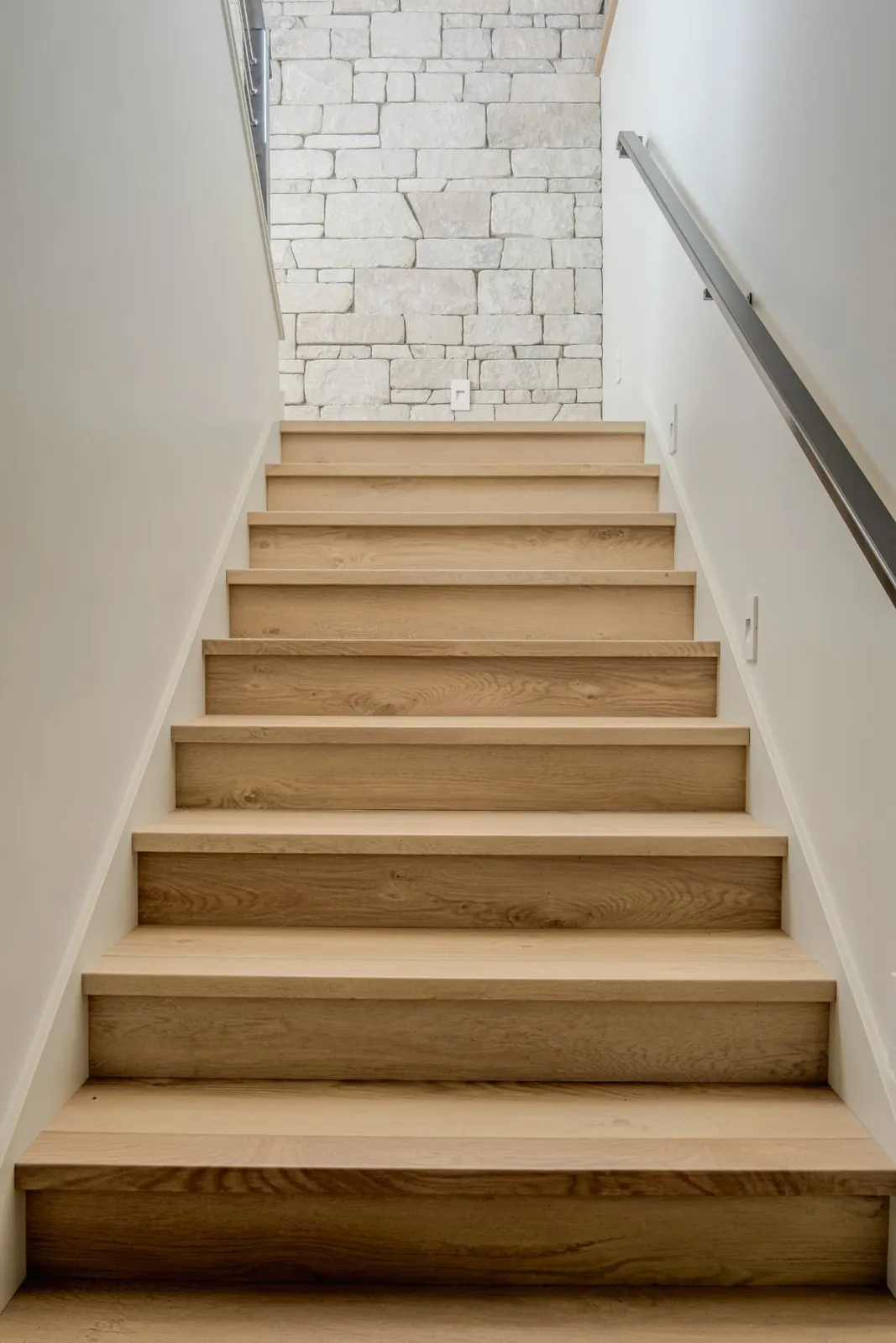 Straight white oak stair flight rising toward a stone wall