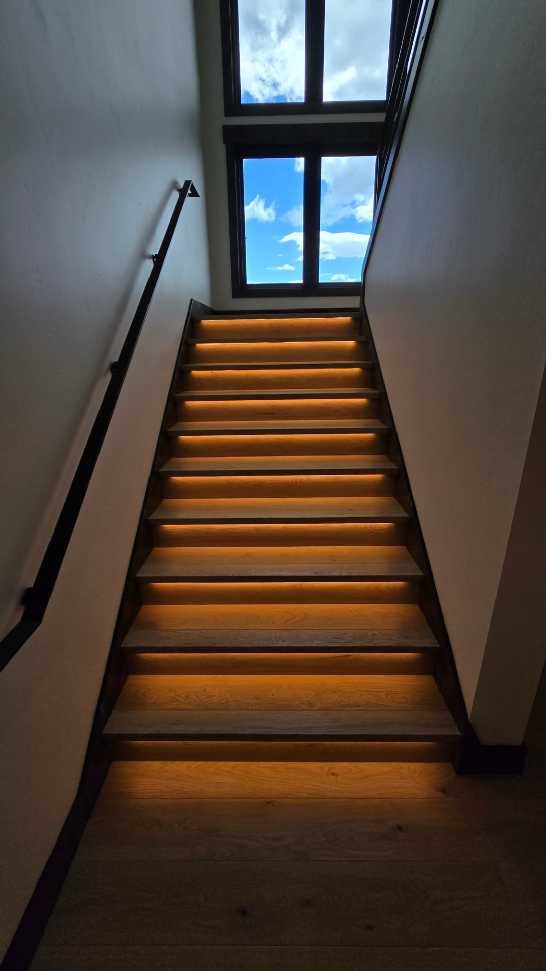 Warm LED-lit stair run rising toward a tall window
