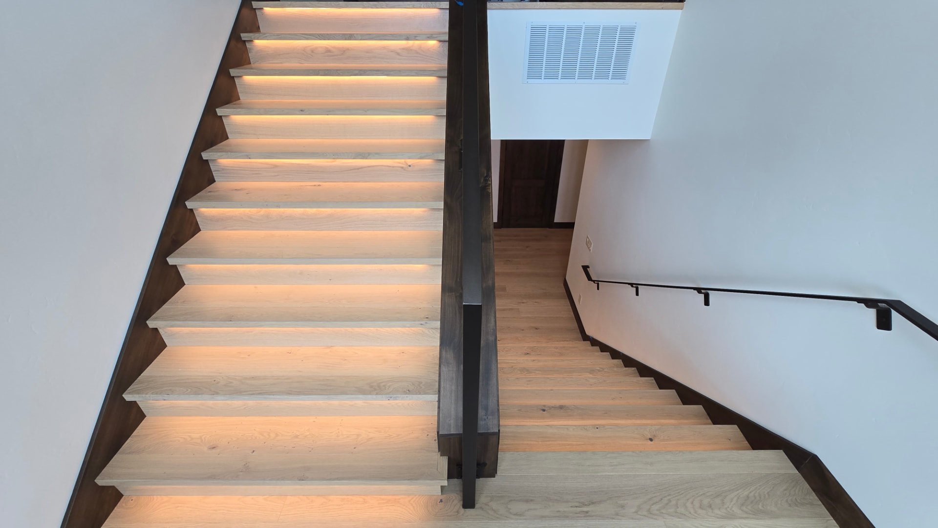 Backlit white oak stair run viewed from the landing above